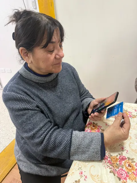 Una mujer mayor mira su teléfono mientras sostiene la credencial +Cerca.