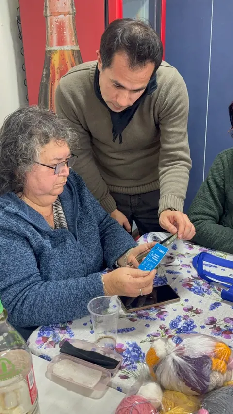 Una mujer mayor y un hombre junto a una mesa con teléfonos y credenciales +Cerca.