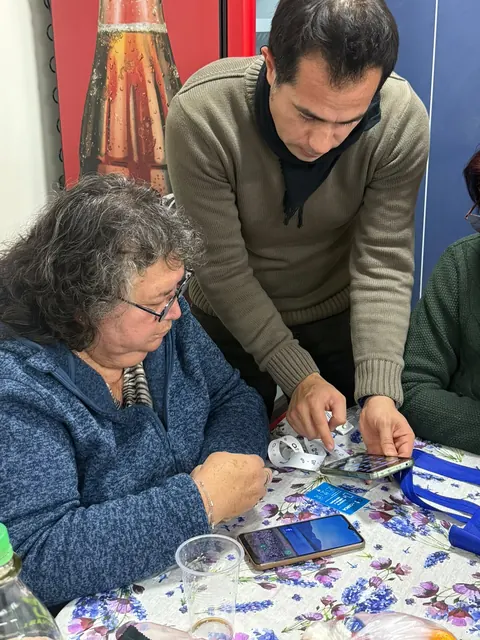 Una mujer mayor y un hombre de pie revisan una credencial +Cerca junto a un teléfono.
