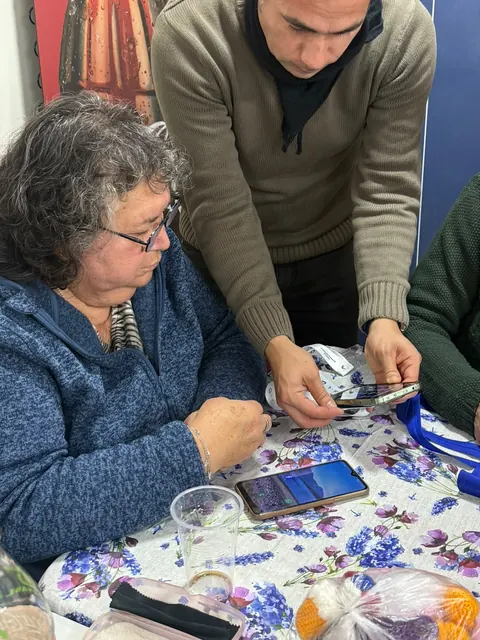 Una mujer mayor revisa su teléfono junto a la credencial +Cerca, con un hombre que la acompaña.