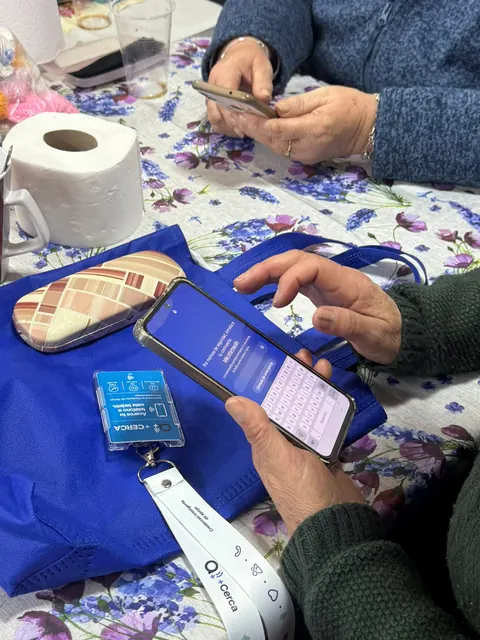 Credencial +Cerca con su lanyard junto a un teléfono sobre una bolsa azul.
