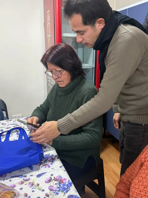 Una mujer mayor sentada y un hombre que le explica cómo usar la credencial +Cerca en su teléfono.