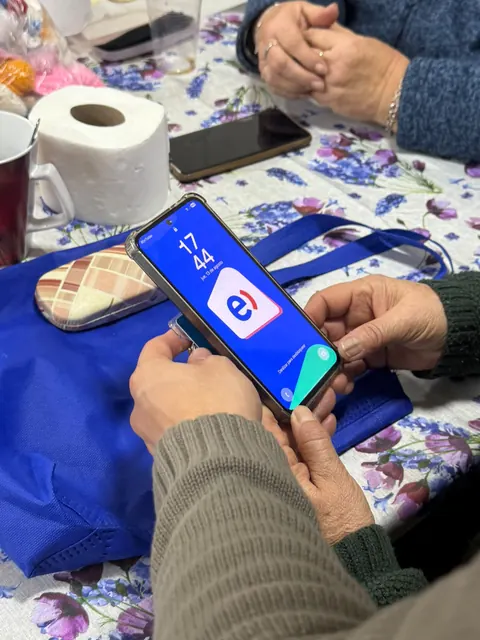 Manos sostienen un teléfono con la pantalla encendida sobre una bolsa azul.